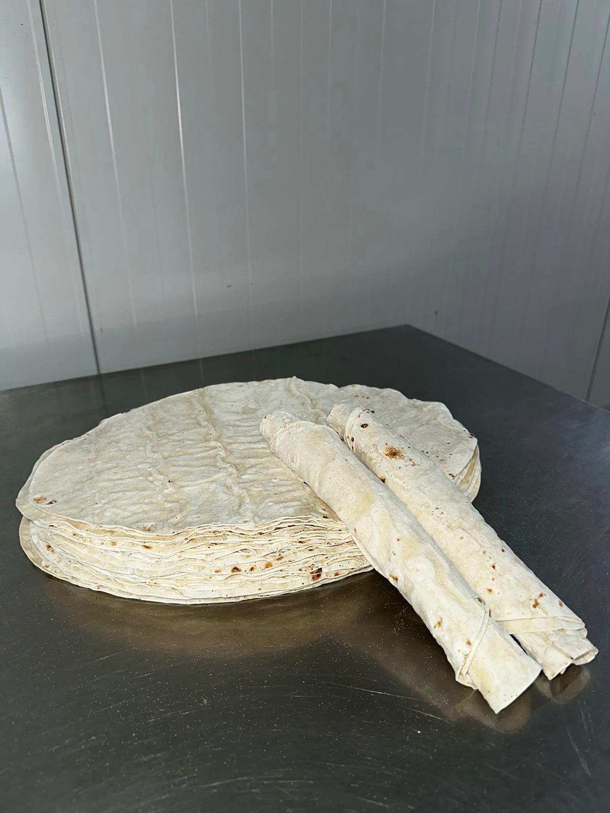 Stapel ronde yufka met twee opgerolde d&uuml;r&uuml;m erop, op een roestvrijstalen werktafel in de productieruimte